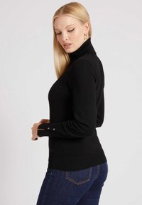 Maglione a collo alto nero con maniche lunghe, caratterizzato da dettagli a pressione visibili ai polsi e una silhouette aderente, completato da una texture liscia.