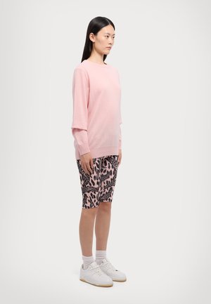 Light pink knitted sweater with long sleeves, paired with black and pink leopard print bike shorts, and white sneakers with a textured sole.