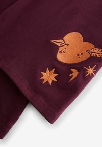 Bordová látka s oranžovými vyšívanými motívmi srdca a hviezdy; má hladkú textúru a priliehavý strih s čistými hranami.