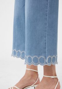 Helle blaue Denim-Hosen mit weitem Bein und weißem, gewelltem Spitzenbesatz am Saum. Sie weisen eine glatte Textur und eine lässige Passform auf.