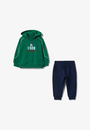 Grüner Hoodie mit weißen Akzenten und Mickey-Mouse-Grafik; kombiniert mit dunkelblauen Jogginghosen mit elastischem Bund und Taschen.