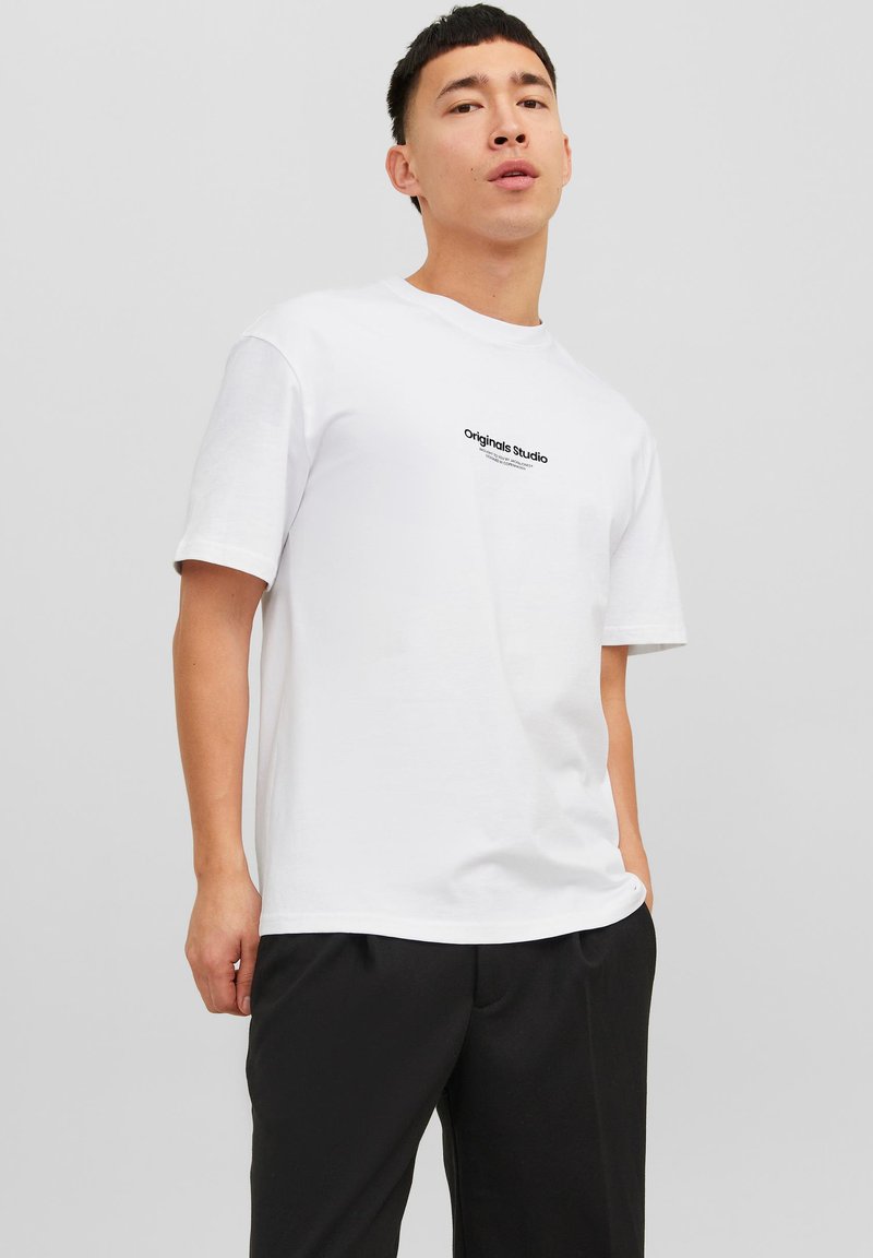 Relaxed-fit white t-shirt with short sleeves, featuring a black "Originals Studio" logo printed on the chest in a standard font.