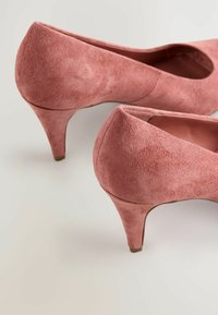 Rosa Wildlederschuhe mit hohen Absätzen, runder Zehenform und spitz zulaufendem Absatz. Die Textur ist weich, mit einem glatten Innenfutter und dezenten Nähdetails.