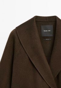 Bruine wollen jas met een brede revers en een gladde textuur. Het binnenlabel vermeldt "Massimo Dutti." Eenvoudig ontwerp, zonder opvallende patronen of accenten.