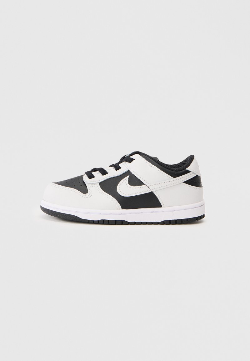 Niske crno-bijele Nike tenisice s vezicom sprijeda i bijelim Swoosh logotipom sa strane, prikazane u profilu na jednobojnoj pozadini.