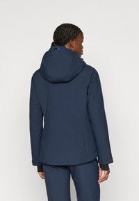 Chaqueta impermeable de color navy con capucha ajustada, cierre de cremallera y puños elásticos. Textura suave con un logo sutil cerca del dobladillo.