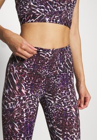 Fioletowy i czarny wzorzysty strój sportowy składający się z dopasowanej crop top i legginsów o wysokim stanie, charakteryzujących się gładką, elastyczną teksturą.