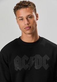 Fekete pulóver ezüst szegecsekkel díszített AC/DC logóval. Bordás nyak és mandzsetta, puha tapintás, laza fazon.