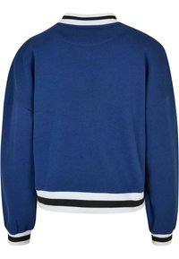 Sudadera azul con cuello y puños a rayas blancas y negras acanalados. Presenta un ajuste cuadrado y una textura suave. Vista trasera mostrada.