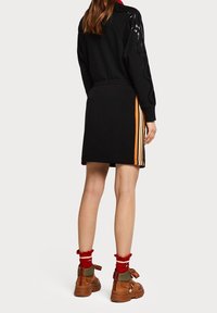 Zwarte sweatshirt en rok met oranje strepen; bruine chunky enkellaarsjes met linten; gelaagde rode en witte sokken.