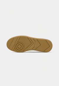 Semelle de chaussure en caoutchouc beige avec des motifs circulaires et en chevrons sur un fond gris clair.