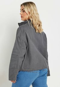 Chaqueta de pana gris con cuello alto, hombros caídos y bajo deshilachado, combinada con jeans azules. La tela tiene un acabado suave y texturizado.