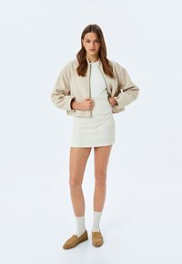 Beige cropped jasje, witte aansluitende top, textuur witte mini rok, lichtbruine loafers en witte sokken. Glad stof, gestructureerd ontwerp.