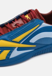 Blue and yellow athletic shoe featuring a textured mesh upper, combined with a red knit collar and synthetic accents for durability.
