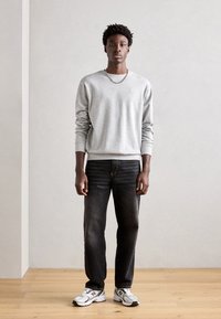 Sudadera gris con escote redondo, combinada con jeans de mezclilla oscuros. Zapatillas en blanco y negro con un logo, sobre un fondo claro.