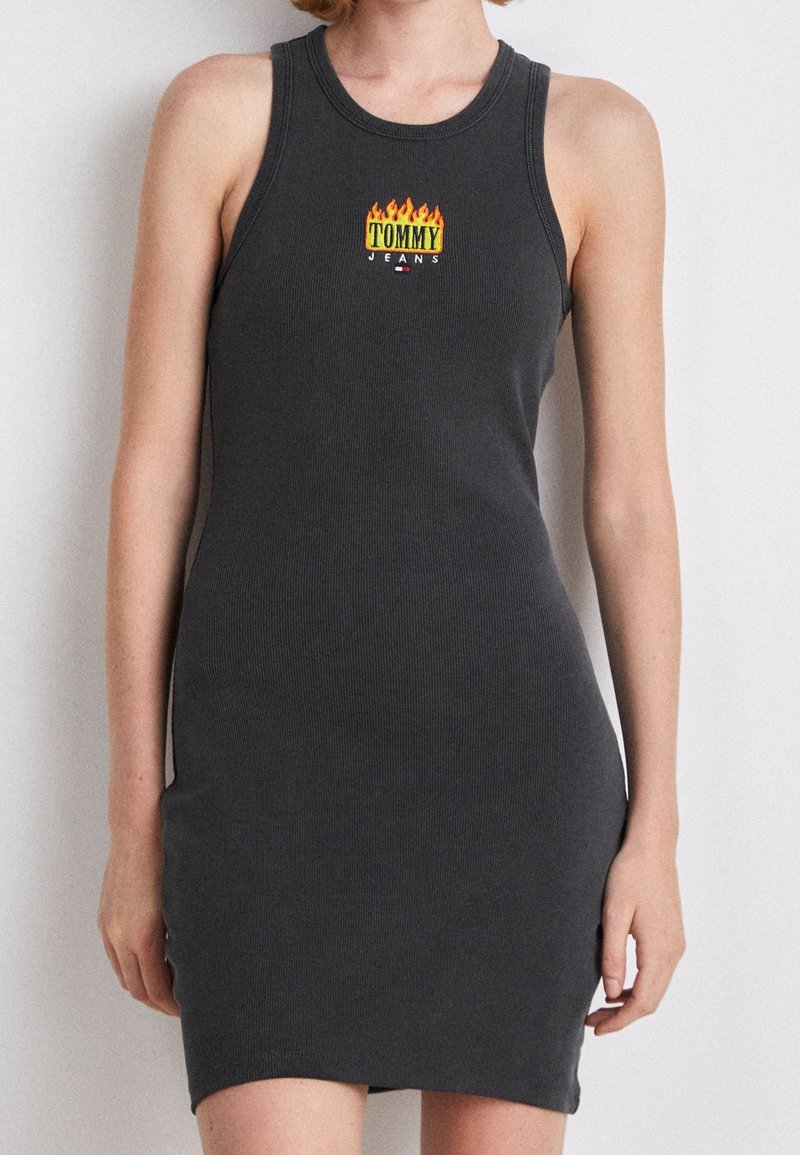 Robe débardeur côtelée gris foncé avec une silhouette ajustée. Présente un logo coloré "TOMMY JEANS" avec des flammes sur la poitrine.
