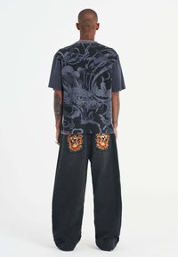 Black graphic t-shirt featuring a dragon print on the back, paired with loose dark denim jeans and embroidered skull patches on pockets.