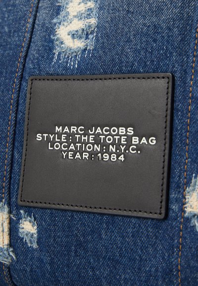 Borsa a spalla in denim con una texture invecchiata, dotata di un'etichetta in pelle nera con la scritta "Marc Jacobs", "The Tote Bag", "N.Y.C." e "1984".