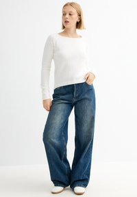 Suéter blanco de punto con un escote cuadrado, combinado con unos pantalones vaqueros de mezclilla azul de corte holgado. Los pantalones son de talle alto y tienen un acabado desvaído.