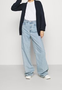 Granatowy kardigan z otwartym przodem, długie rękawy, noszony na białej koszuli i jasnoniebieskich jeansach z szerokimi nogawkami i wysokim stanem, uzupełniony białymi trampkami.