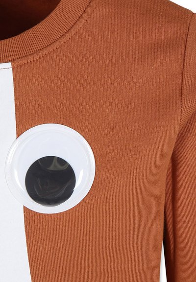 Maglione marrone a coste con un design circolare a forma di occhio in plastica con un centro nero sul lato sinistro e un pannello bianco per contrasto.