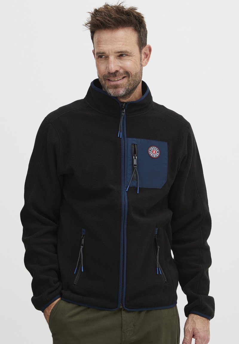 Chaqueta de forro polar negra con un bolsillo en el pecho de color navy, cierre delantero con cremallera y acentos azules. Presenta bolsillos laterales y un cuello alzado.