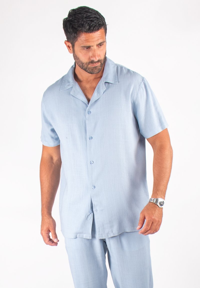 Chemise à manches courtes bleu clair avec boutons, en tissu doux, au design décontracté, avec un col à revers et une texture lisse.