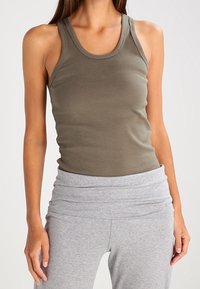 Camiseta sin mangas de color verde oliva con cuello redondo y ajuste ceñido, acompañada de leggings gris claro con una cinturilla en capas. Material suave y elástico.