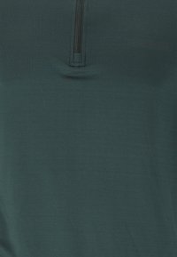 Tissu en polaire vert foncé avec une fermeture éclair verticale noire au centre, près du col supérieur.