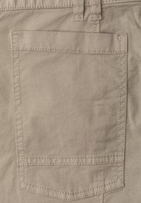 Béžová látková kapsa na kalhotách s viditelným stehem a průvlekem na pásek nahoře, zobrazující texturu a švy zblízka.