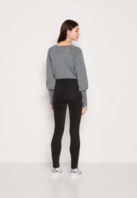 Sivi pulover s raglan rukavima, sparen s crnim trapericama visokog struka. Model nosi sive i bijele tenisice. Jednostavna pozadina.