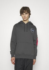 Sudadera de algodón gris con bolsillo frontal, capucha con cordón, logo de la NASA en el pecho y bolsillo con cremallera de acento rojo en la manga izquierda.