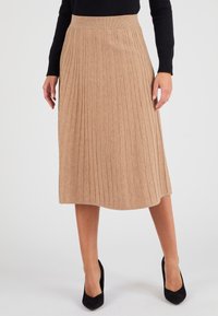 Gonna plissettata beige realizzata in tessuto morbido, dotata di una cintura a coste e di una lunghezza fino a metà polpaccio con una texture liscia. Scarpe con tacco alto nere.