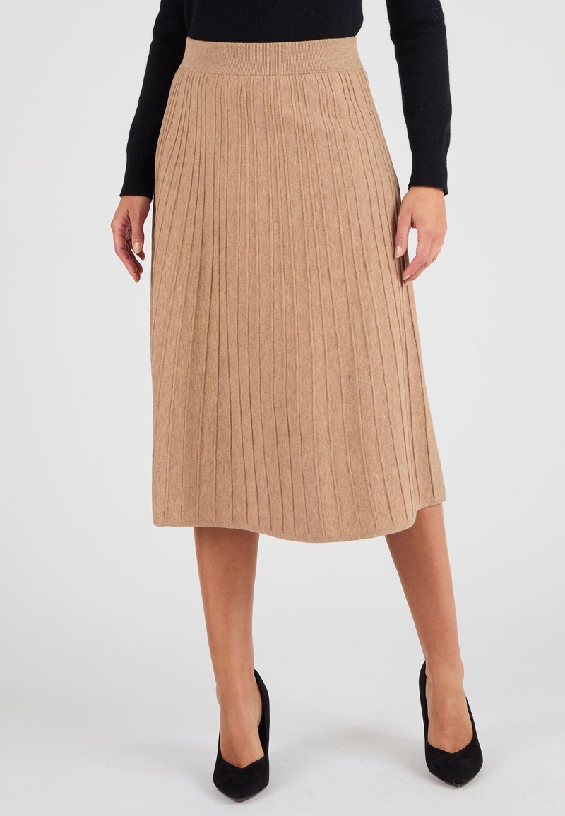 Gonna plissettata beige realizzata in tessuto morbido, dotata di una cintura a coste e di una lunghezza fino a metà polpaccio con una texture liscia. Scarpe con tacco alto nere.