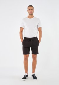 T-shirt bianca a maniche corte e pantaloni corti neri con cordoncino, dal taglio rilassato, abbinati a scarpe da ginnastica nere e bianche. Design minimale.