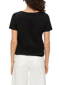 Zwarte t-shirt met een relaxte pasvorm, korte mouwen en een wijde halslijn, gecombineerd met hoge taille witte wijde jeans.