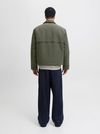 Khaki groene jas met een brede kraag, rugpand detail en geribbelde zoom, gecombineerd met losse marineblauwe broeken voor een comfortabele pasvorm.