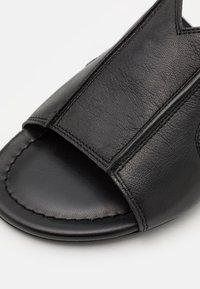 Nära bild av en svart läder öppen tå slide sandal med texturerad ovandel och sydda detaljer på sulan.