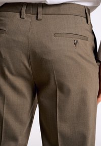 Bruine broeken met een gladde textuur, op maat gemaakt ontwerp met twee achterzakken en een knoopaccent. Klassieke stijl met platte voorkant.
