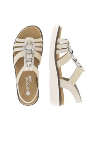 Sandalo beige con più cinture in tessuto e un accento metallico circolare. Presenta una soletta imbottita e una suola esterna bianca texturizzata.