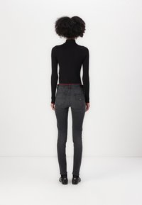 Černý žebrovaný rolák s dlouhými rukávy, spojený s tmavě šedými skinny džíny a černými botami, z pohledu zezadu.