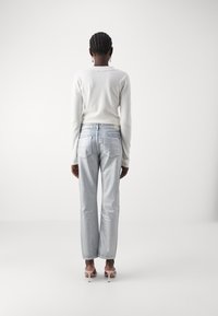 Suéter blanco de manga larga, jeans rectos azul claro con bolsillos traseros y sandalias de tacón rosa pálido, visto desde la parte trasera.