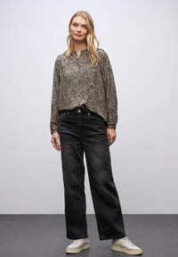 Blusa a maniche lunghe, di taglio ampio, con stampa leopardata in beige e nero; abbinata a jeans neri a vita alta e gamba larga e scarpe da ginnastica chiare.