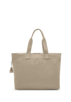 Bolso tote beige con asas dobles, un parche de logo circular en el centro y un pequeño llavero de mono sujeto a la cremallera del lado izquierdo.