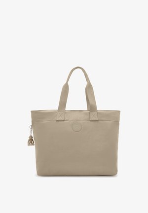 Bolso tote beige con asas dobles, un parche de logo circular en el centro y un pequeño llavero de mono sujeto a la cremallera del lado izquierdo.