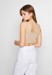 Top cropped canelado bege com alças largas e costas arredondadas, combinado com calças brancas de cintura alta. Textura suave, design minimalista.