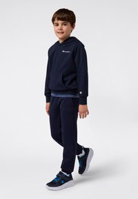 Marineblauw sweatshirt en joggers set, met een voorkant zak, ribbel manchetten en geborduurd logo; gecombineerd met marineblauwe en witte sneakers.