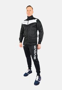 Black tracksuit with white accents, featuring a zip-up jacket and fitted pants. Material is smooth, with GIVOVA branding on the side.