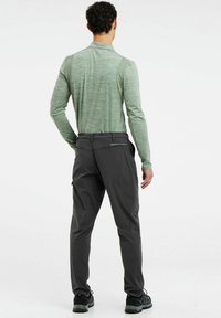 Mannen sportoutfit met een lichtgroen shirt met lange mouwen en donkergrijze broek. De materialen zijn ademend met een slim fit en functionele zakken.
