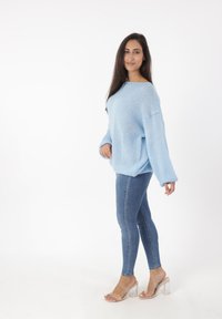 Lichtblauwe oversized trui met een gestructureerd breipatroon, gecombineerd met strakke blauwe jeans en heldere blokhaksandalen.